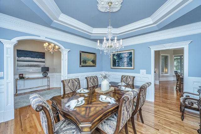 dining room with ornamental molding, a tray ceiling, light wood-type flooring, and decorative columns