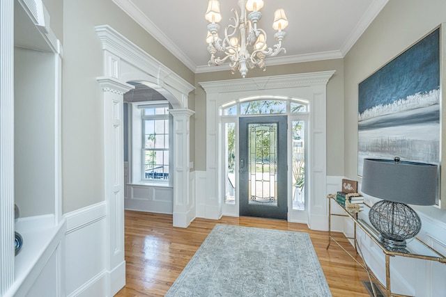 foyer featuring a notable chandelier, ornate columns, crown molding, and light hardwood / wood-style flooring