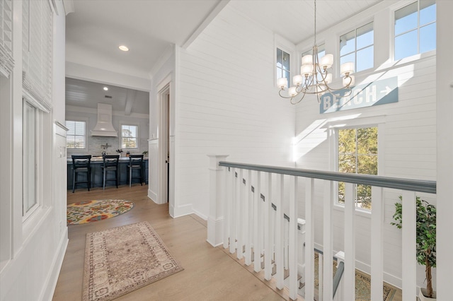 hallway featuring light hardwood / wood-style flooring, beamed ceiling, and a chandelier