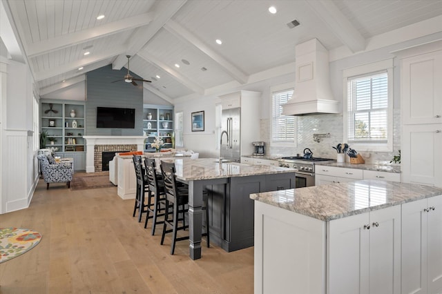 kitchen with light stone countertops, custom range hood, a large island with sink, light hardwood / wood-style flooring, and white cabinets