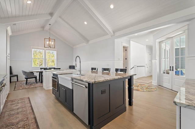 kitchen with white cabinetry, french doors, stainless steel appliances, light stone counters, and an island with sink