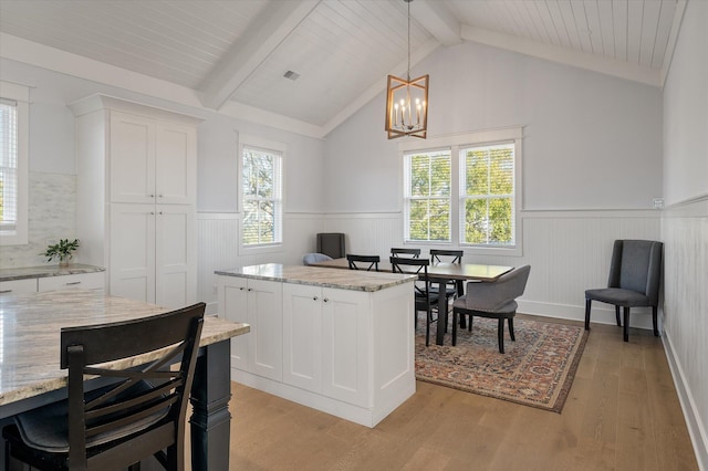 kitchen with pendant lighting, lofted ceiling with beams, a center island, light hardwood / wood-style floors, and white cabinetry