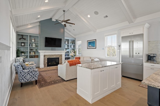 living room featuring built in shelves, ceiling fan, light hardwood / wood-style flooring, lofted ceiling with beams, and a fireplace