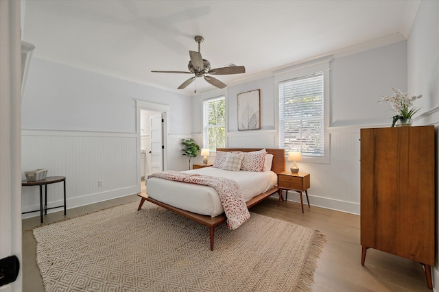 bedroom featuring ceiling fan, light wood-type flooring, ornamental molding, and ensuite bath