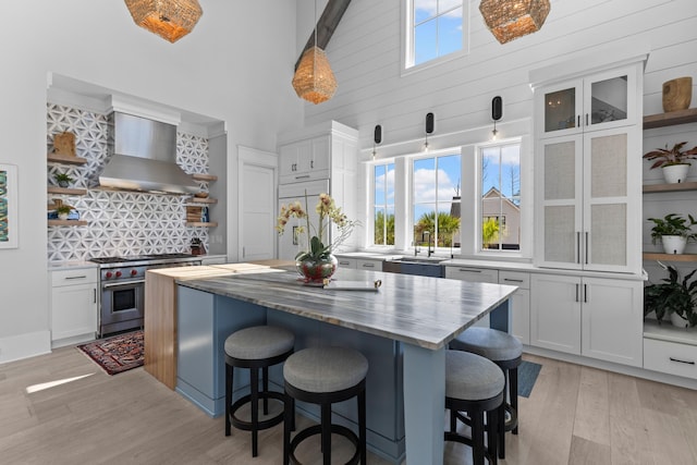 553 Old Compass Rd, Daniel Island, SC 29492 - kitchen featuring open shelves, wall chimney range hood, high end stove, light wood finished floors, and a high ceiling