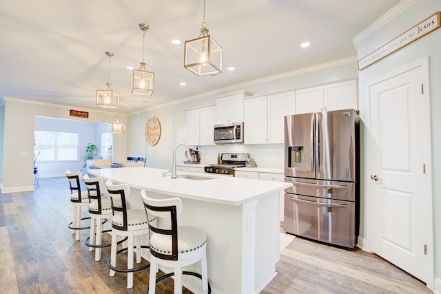 kitchen with a center island with sink, white cabinets, hanging light fixtures, and appliances with stainless steel finishes