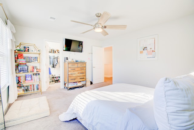 bedroom featuring a walk in closet, light colored carpet, a closet, and ceiling fan