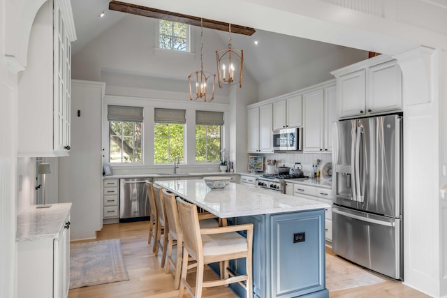 kitchen featuring white cabinetry, hanging light fixtures, a kitchen island, stainless steel appliances, and light stone countertops