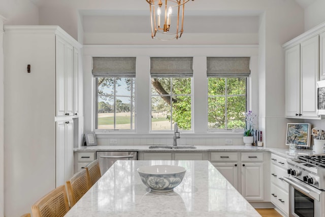 kitchen with appliances with stainless steel finishes, decorative light fixtures, sink, white cabinets, and light stone countertops