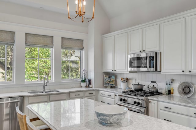 kitchen with pendant lighting, sink, stainless steel appliances, light stone counters, and white cabinets