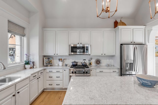 kitchen with sink, light hardwood / wood-style flooring, hanging light fixtures, stainless steel appliances, and white cabinets