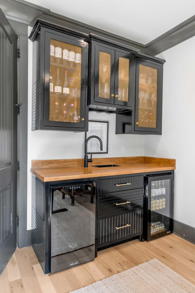 bar with wood counters, sink, light hardwood / wood-style floors, and beverage cooler