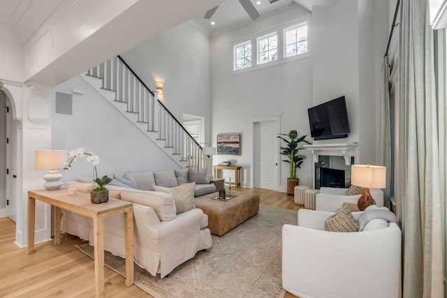 living room featuring hardwood / wood-style flooring, a towering ceiling, ornamental molding, and a fireplace