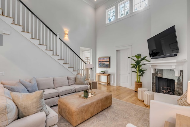 living room with a premium fireplace, ornamental molding, a high ceiling, and light hardwood / wood-style flooring