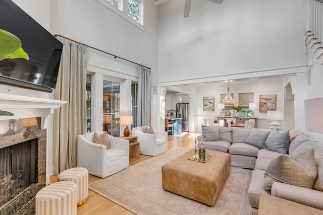 living room featuring a towering ceiling, wood-type flooring, a premium fireplace, and ceiling fan