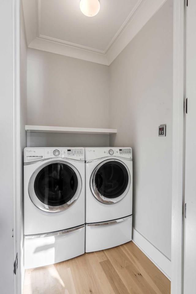 clothes washing area with ornamental molding, wood-type flooring, and washing machine and clothes dryer