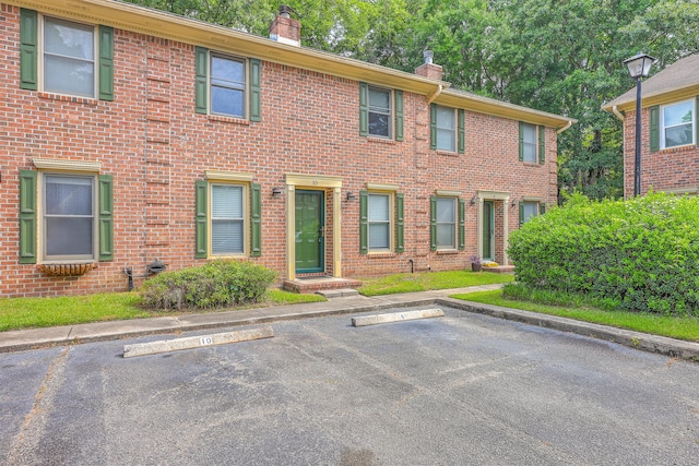 view of front of house featuring a chimney, uncovered parking, and brick siding