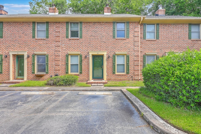 view of front of home with a chimney, uncovered parking, and brick siding
