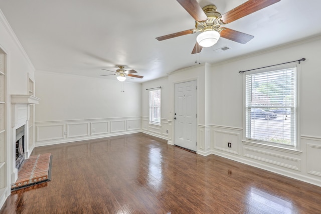 unfurnished living room featuring a ceiling fan, crown molding, a fireplace, wainscoting, and wood finished floors