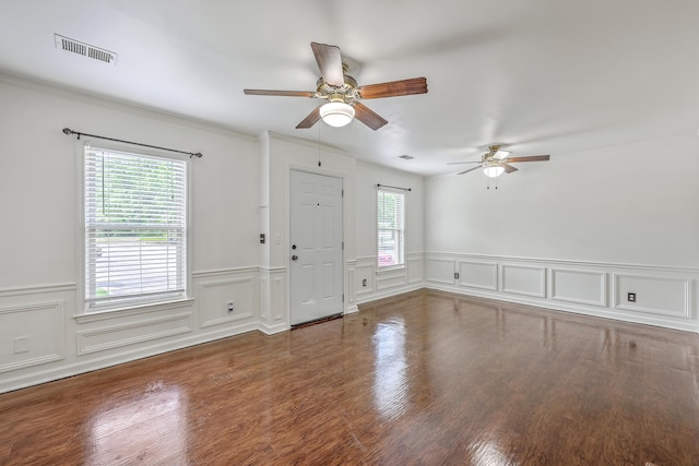 empty room featuring a ceiling fan, a wainscoted wall, crown molding, wood finished floors, and a decorative wall