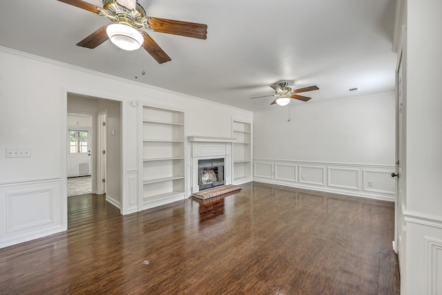 unfurnished living room with ceiling fan, built in shelves, ornamental molding, dark wood-style floors, and a brick fireplace