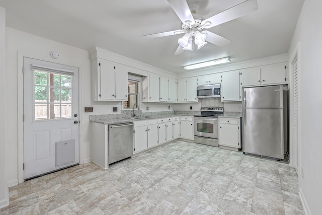 kitchen featuring stainless steel appliances, a sink, a ceiling fan, baseboards, and white cabinets