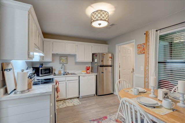 kitchen featuring white cabinets, appliances with stainless steel finishes, light wood finished floors, and a sink