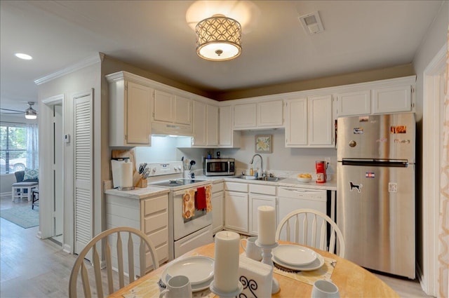 kitchen with a sink, under cabinet range hood, white cabinetry, light countertops, and appliances with stainless steel finishes