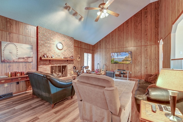 living room featuring wood walls, light hardwood / wood-style flooring, ceiling fan, and a brick fireplace