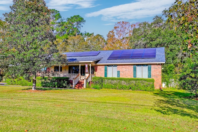 ranch-style house featuring solar panels, covered porch, and a front yard