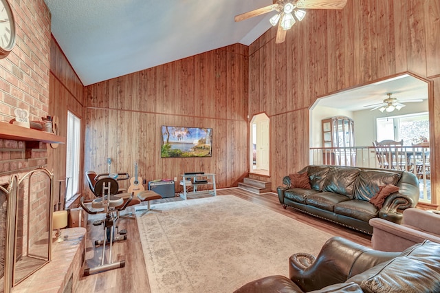 living room with wooden walls, ceiling fan, high vaulted ceiling, and light hardwood / wood-style flooring