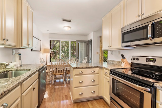 kitchen with light wood-type flooring, kitchen peninsula, light stone countertops, appliances with stainless steel finishes, and sink