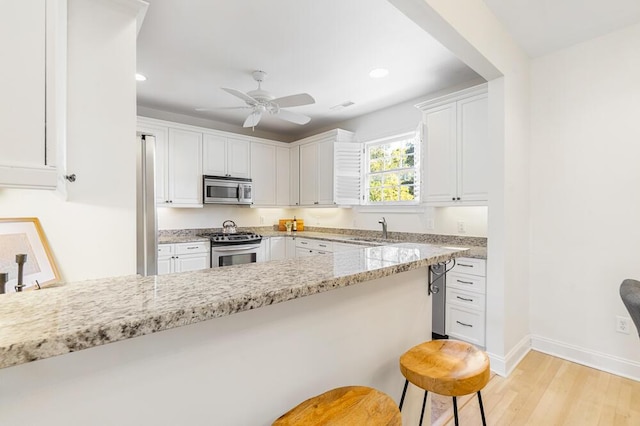 kitchen featuring appliances with stainless steel finishes, light stone countertops, white cabinets, a breakfast bar, and sink