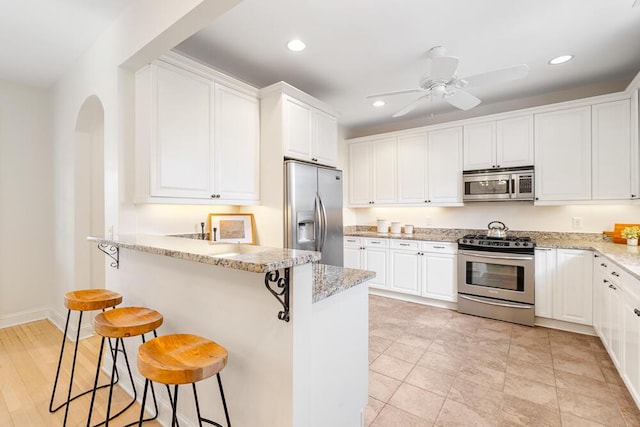 kitchen with ceiling fan, white cabinets, appliances with stainless steel finishes, and a breakfast bar area