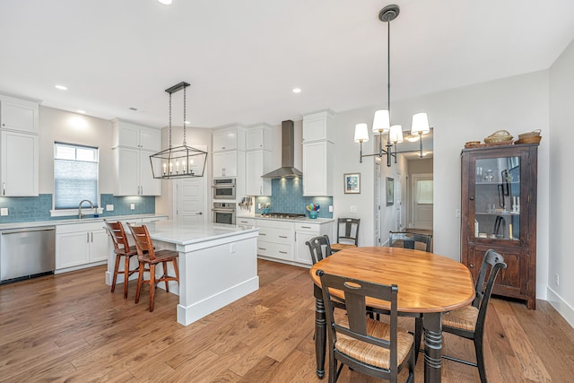 kitchen featuring light countertops, wall chimney exhaust hood, appliances with stainless steel finishes, and a chandelier
