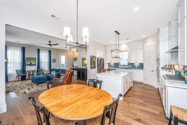 dining room with visible vents, a healthy amount of sunlight, ceiling fan with notable chandelier, and light wood-style floors