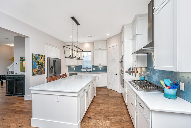 kitchen with a kitchen island, wall chimney range hood, white cabinets, a sink, and appliances with stainless steel finishes