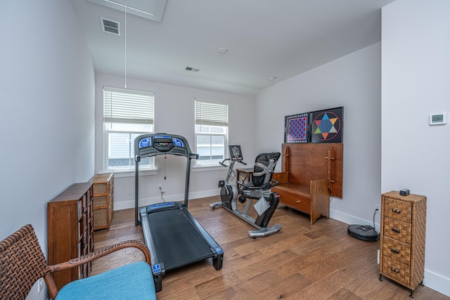 exercise area featuring baseboards, visible vents, wood finished floors, and attic access