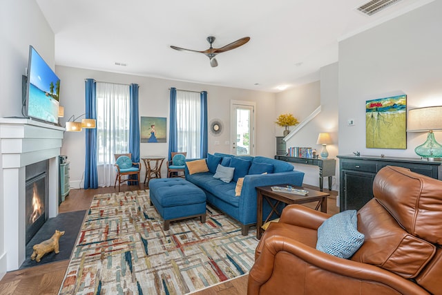 living area with a ceiling fan, visible vents, a glass covered fireplace, and a wealth of natural light