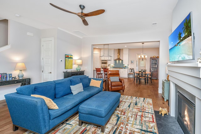 living room featuring visible vents, a fireplace with flush hearth, a ceiling fan, and wood finished floors