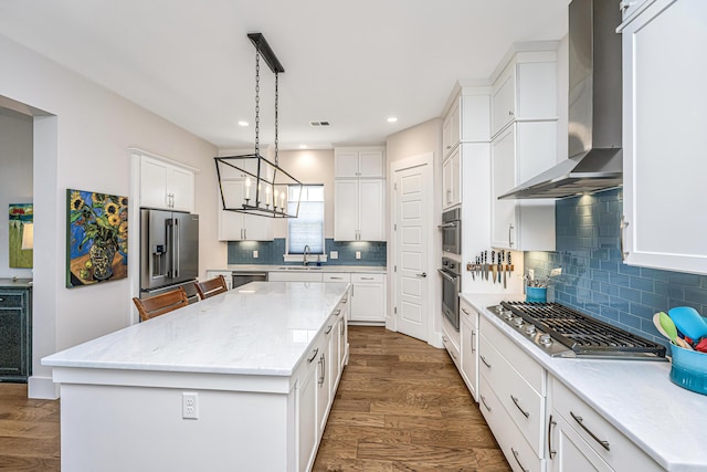 kitchen featuring wall chimney range hood, a kitchen island, appliances with stainless steel finishes, a sink, and dark wood-type flooring