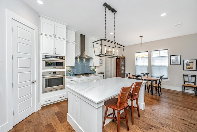 kitchen featuring decorative backsplash, a kitchen island, wall chimney exhaust hood, a notable chandelier, and stainless steel appliances
