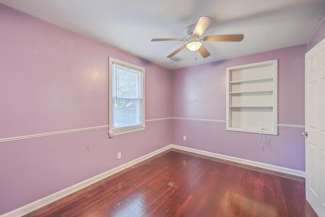 unfurnished room featuring built in shelves, ceiling fan, and dark hardwood / wood-style flooring