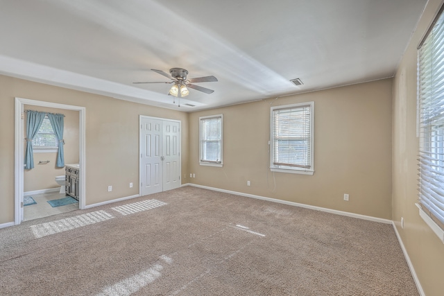 unfurnished bedroom featuring light carpet, a closet, ensuite bathroom, and ceiling fan