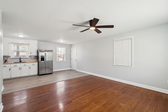 kitchen featuring wood finished floors, a sink, white cabinets, stainless steel refrigerator with ice dispenser, and tasteful backsplash