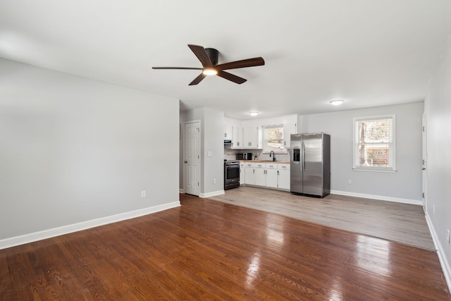 unfurnished living room with a ceiling fan, wood finished floors, baseboards, and a sink