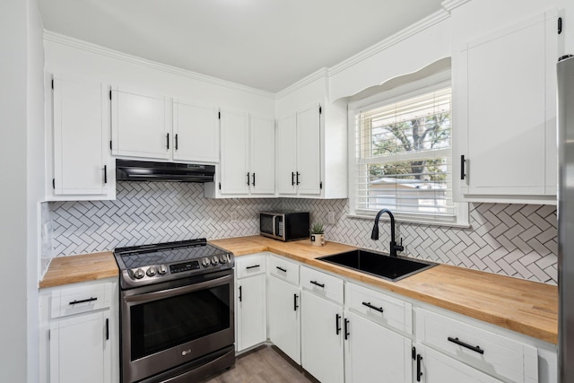 kitchen featuring crown molding, under cabinet range hood, butcher block countertops, stainless steel appliances, and a sink