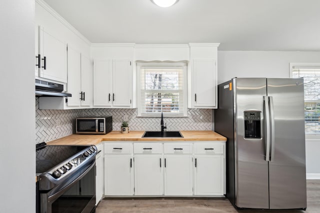 kitchen featuring wooden counters, a sink, stainless steel appliances, under cabinet range hood, and tasteful backsplash