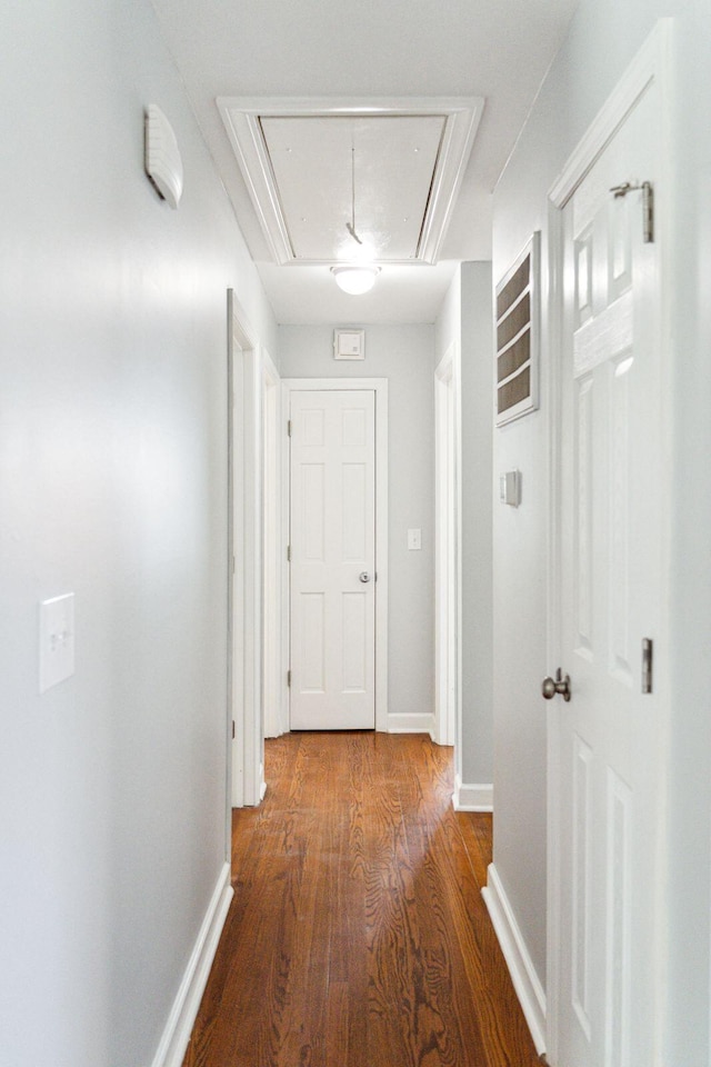 hallway featuring attic access, wood finished floors, and baseboards