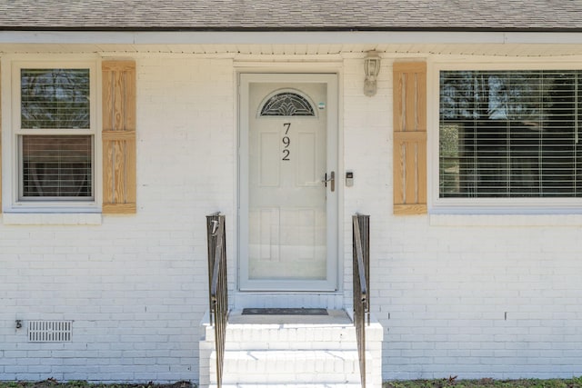 doorway to property with brick siding and a shingled roof